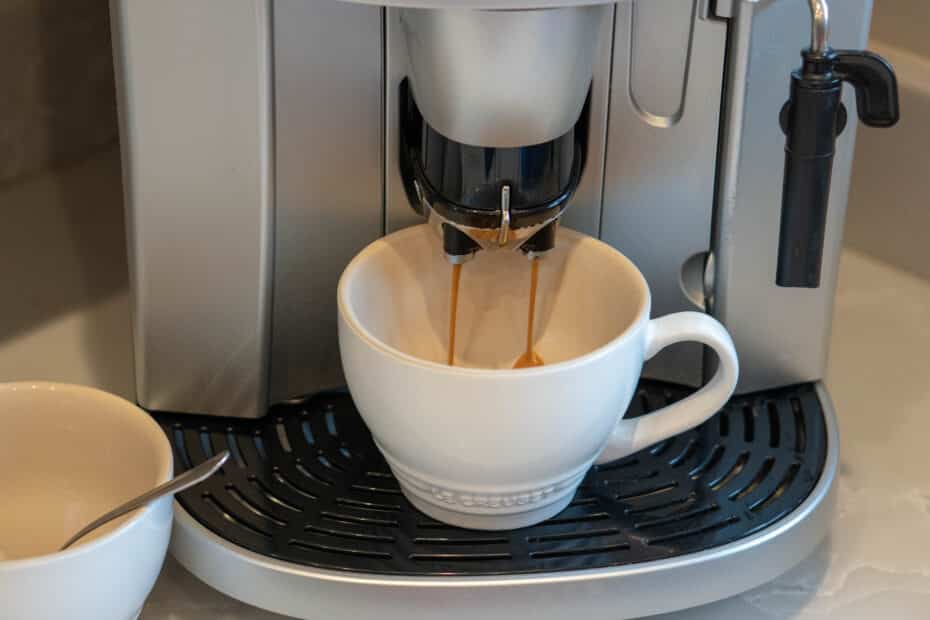 A close-up of a Bosch coffee machine pouring coffee into a white cup placed on the drip tray, with another cup and spoon nearby on the left.