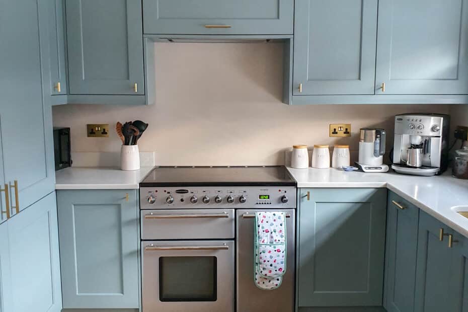 Modern kitchen with light blue cupboards, a stainless steel oven, and wooden floor. Worktops hold kitchen utensils, jars, and a coffee machine—perfect inspiration if you’re seeking tips for buying a house with stylish finishes. A colourful towel hangs on the oven handle.